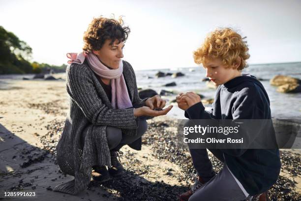 mother and son crouching on the beach - boy exploring on beach stock-fotos und bilder