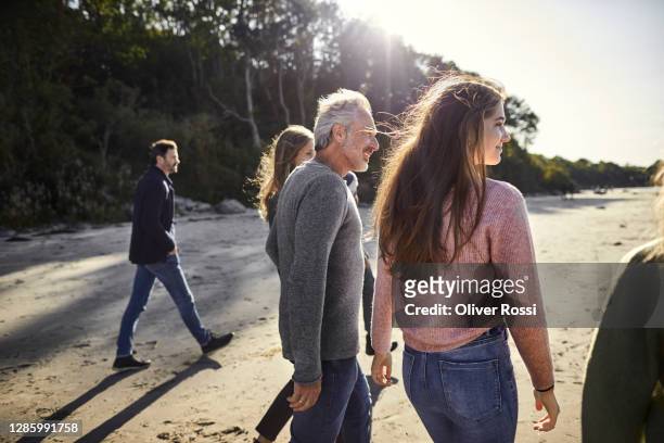 family and friends strolling on the beach - kleine personengruppe stock-fotos und bilder