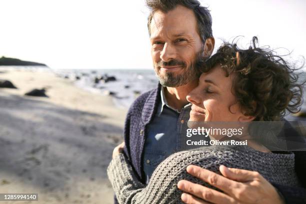 portrait of smiling mature couple embracing on the beach - mature couple stock pictures, royalty-free photos & images