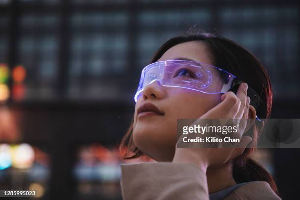 asian woman using a smart glasses in front of an office building - augmented reality woman stock-fotos und bilder