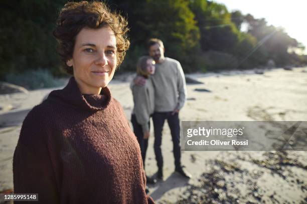 portrait of confident woman on the beach with family in background - depth of field togetherness looking at the camera stock pictures, royalty-free photos & images