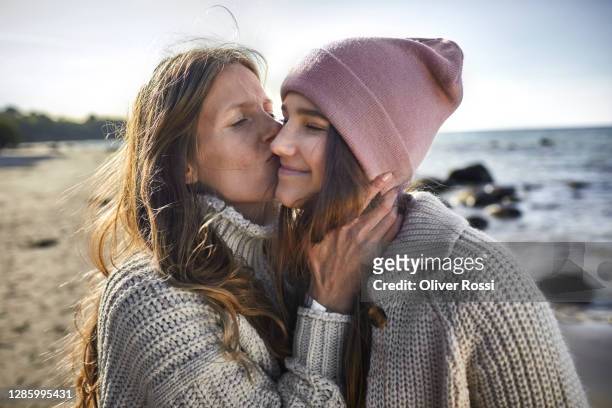 mother kissing daughter on the beach - daughter stock-fotos und bilder