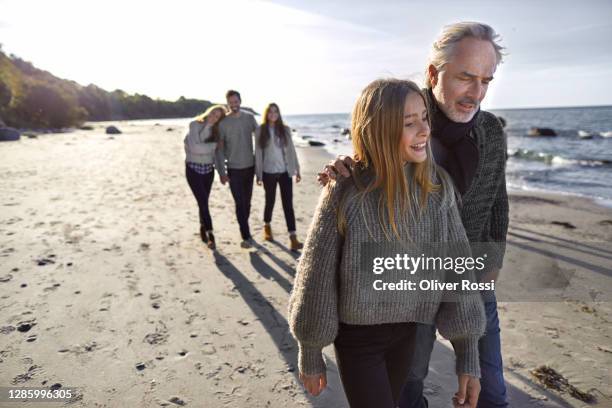 father and daughter strolling on the beach with family in background - young teen girl beach foto e immagini stock