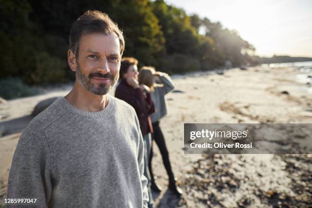 portrait of confident mature man on the beach with family in background - homme content chez lui photos et images de collection