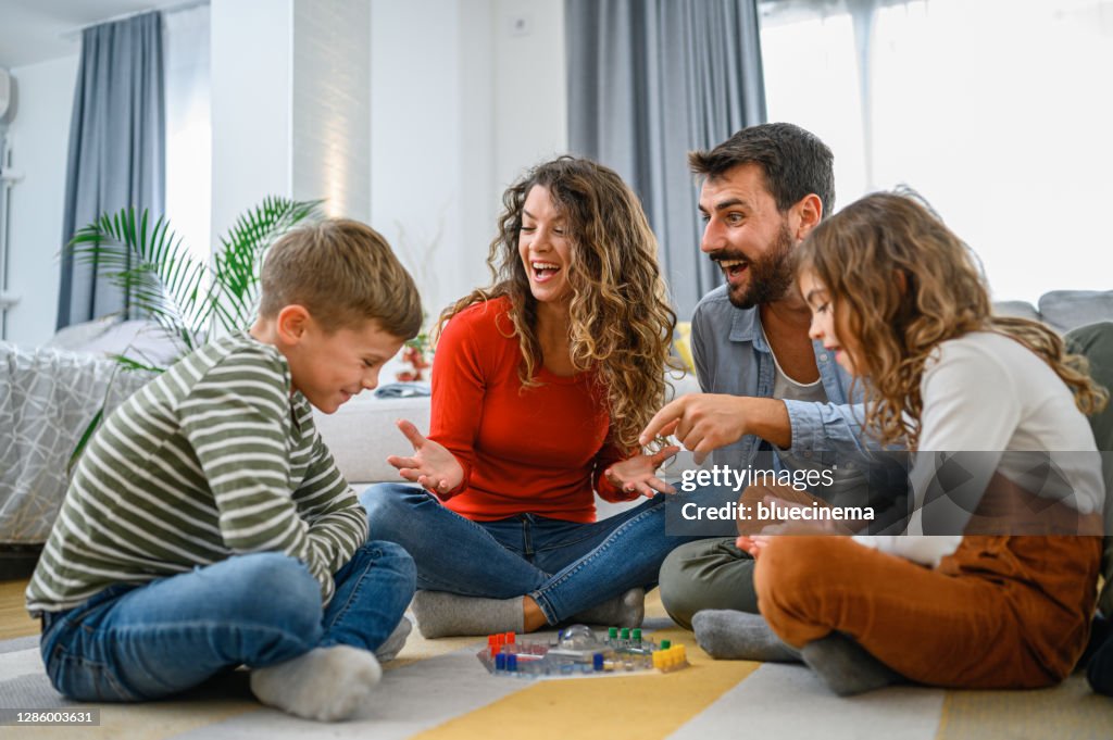 Cheerful parents playing board game with their children.