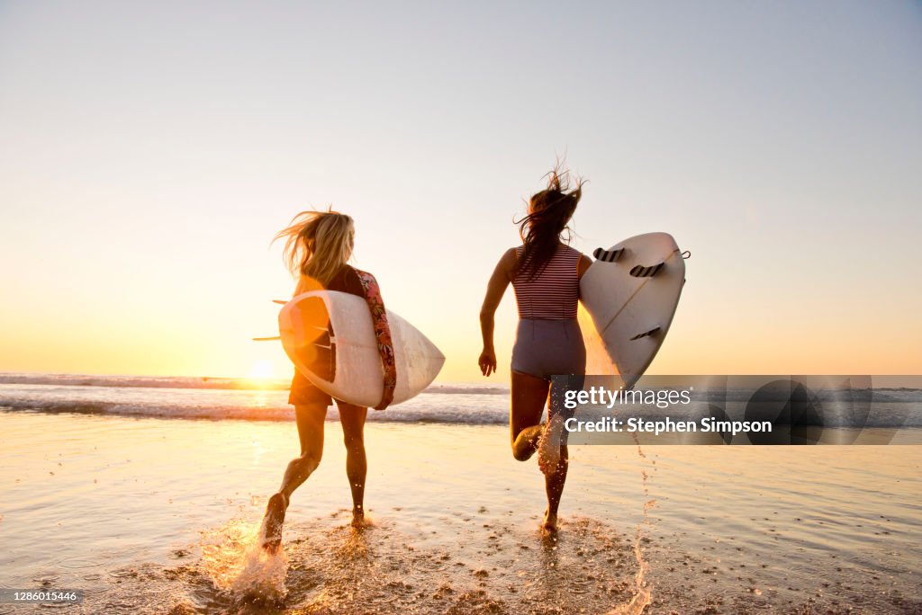 Female surfers running on the beach at sunset