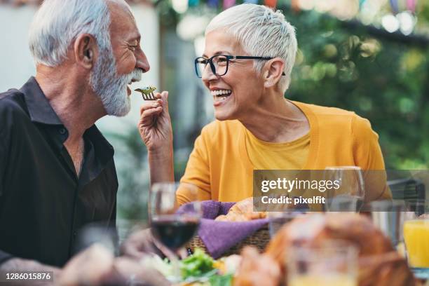 verspielte seniorin füttert ihren mann auf einer gartenparty - best ager paar garten stock-fotos und bilder