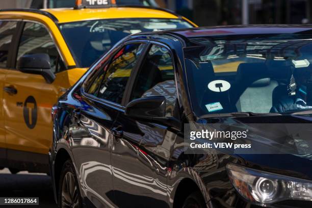 Yellow cabs and Uber car drive through Times Square on November 16, 2020 in New York City. NYC bill is looking to put Uber and yellow Cabs on single...