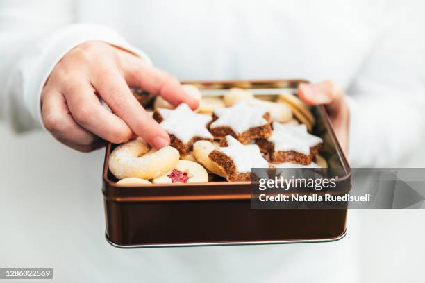 child hand picking up a christmas cookie from the tin box full of traditional cookies baked in switzerland during advent time in december. - child cookie jar stock pictures, royalty-free photos & images