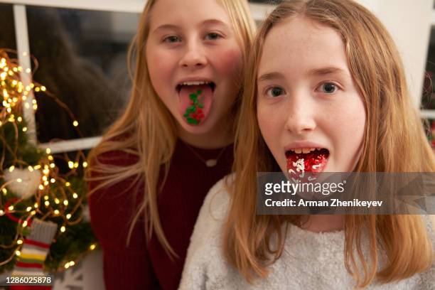 mischievous teenage girls sticking out tongue with sugar sprinkles. having fun while making christmas cookies. - blonde girl sticking out her tongue stock pictures, royalty-free photos & images