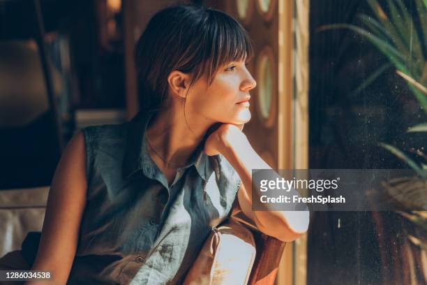 side portrait of a beautiful young woman sitting on a comfy couch at a local cafe and looking through the window - distance stock pictures, royalty-free photos & images