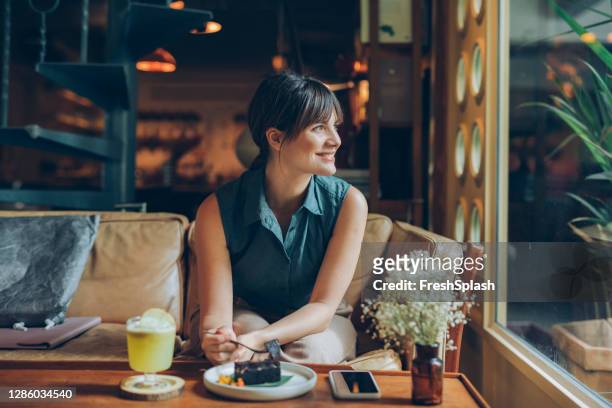 beaufitul sonriente jovencita disfrutando de un pedazo de pastel de chocolate y una copa de limonada fresca en una casa de café acogedora - brownie fotografías e imágenes de stock