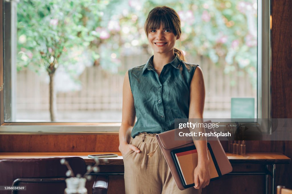 Portrait of a Beautiful Young Businesswoman Holding her Work Essentials, About to Start Working at a Bright Cozy Coffee House