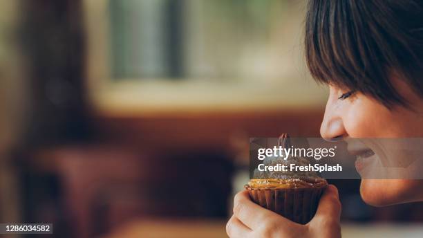 close up: beautiful smiling young woman enjoying the aroma of a delicious looking cupcake - person delicious food stock pictures, royalty-free photos & images