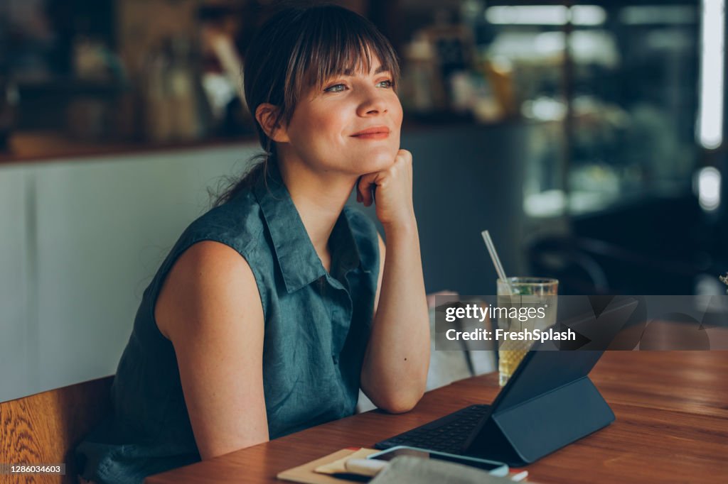 Telecommuting: Beautiful Smiling Young Businesswoman Working Remotely on her Tablet PC from a Cozy Cafe