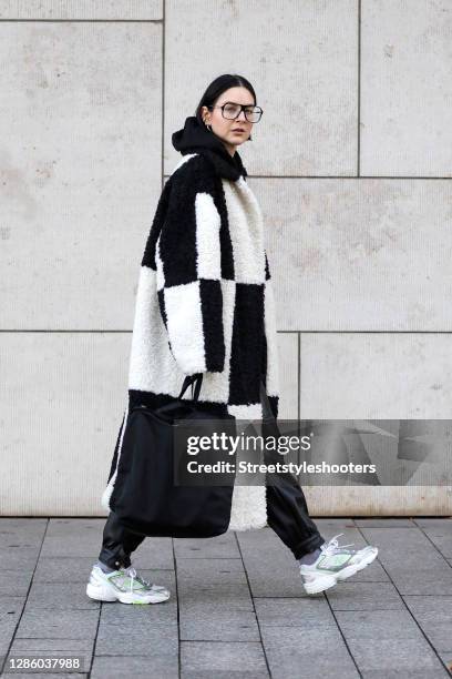 Influencer Maria Barteczko, wearing a black and white checkered faux fur oversized coat by Stand Studio, a black hoodie by Tokio Hotel, black faux...