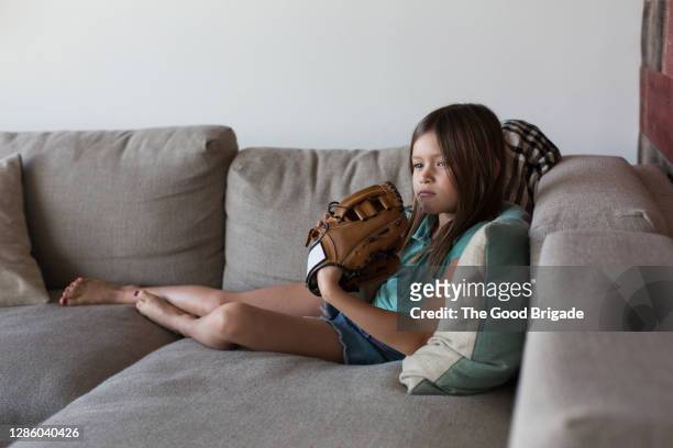 girl sitting on couch wearing baseball glove - baseball glove stock pictures, royalty-free photos & images