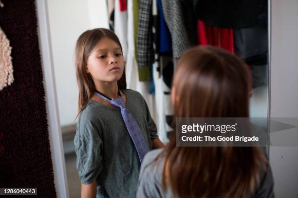 young girl looking at reflection in mirror wearing a neck tie - gender stereotypes stock-fotos und bilder