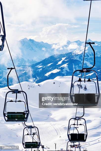 Ski lift with skiers above the slope of snowy Alpine mountains. Sports and recreational background