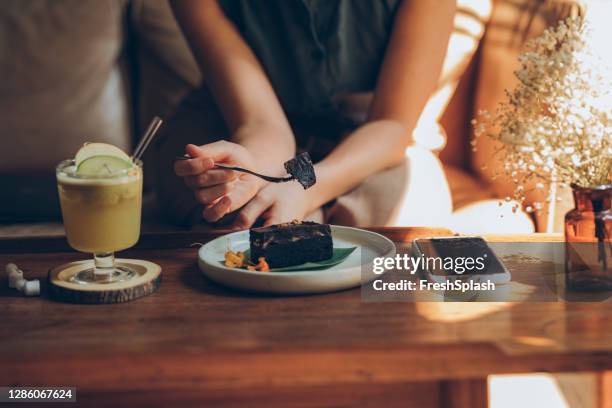 close up: hands of a young woman eating a piece of chocolate cake and having a glass of lemonade at a local cafe - beer mat stock pictures, royalty-free photos & images