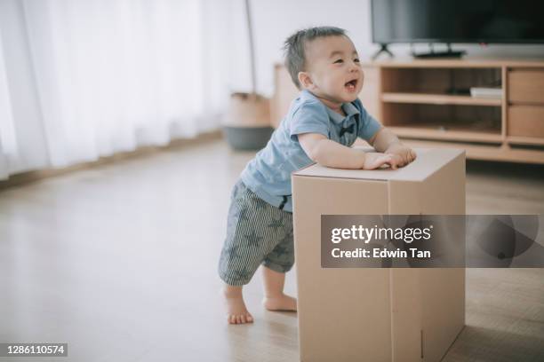 laughing happy asian chinese baby boy playing with carton box in living room looking at his parent - baby standing stock pictures, royalty-free photos & images