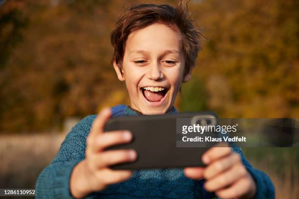 cheerful boy using smart phone while taking selfie - boy taking picture in forest stock-fotos und bilder