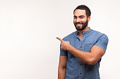 Advertise here! Positive bearded man pointing finger away paying your attention at empty space for advertisement, looking at camera with toothy smile