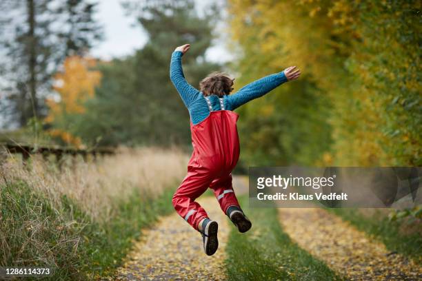 boy jumping on road amidst plants at park - leap forward stock pictures, royalty-free photos & images