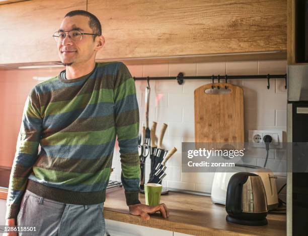 young man with eyeglasses leaning on kitchen counter - thin glass stock pictures, royalty-free photos & images