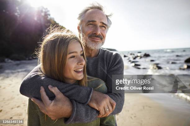 father hugging daughter on the beach - glücklichsein stock-fotos und bilder