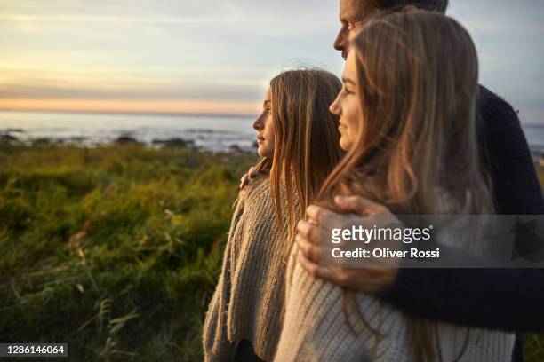 father with two girls looking at view at the sea - contemplation family imagens e fotografias de stock