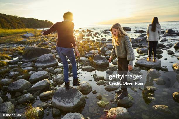 woman and girls balancing on stones at the sea - young teen girl beach foto e immagini stock