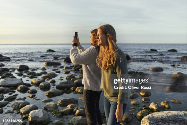 mother and daughter taking smartphone picture at the sea - season 14 stock-fotos und bilder