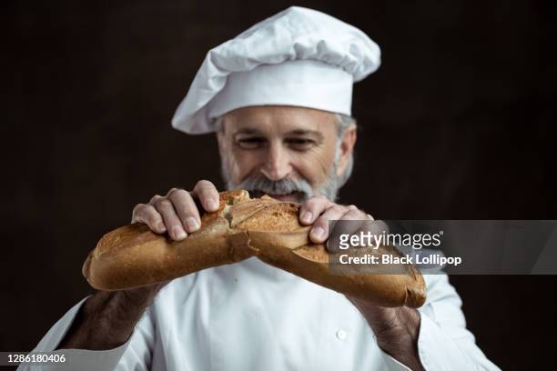 bakery advertisement, portrait of an elderly baker breaking fresh bread - breaking bread stock pictures, royalty-free photos & images