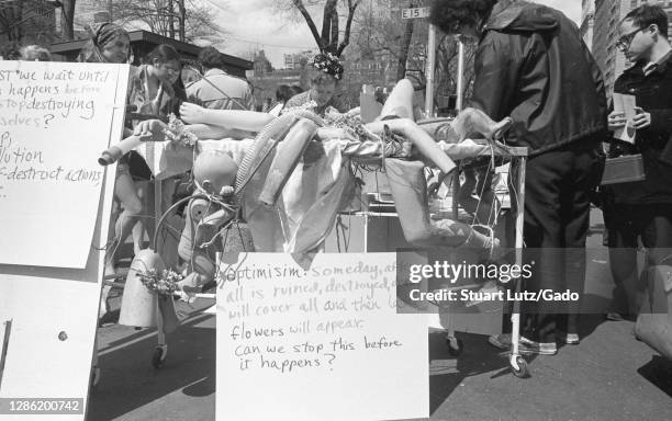 Participants in the first annual Earth Day event, outside on a sunny day, crowd around a trolley containing plastic, wires, and an environmentalist...