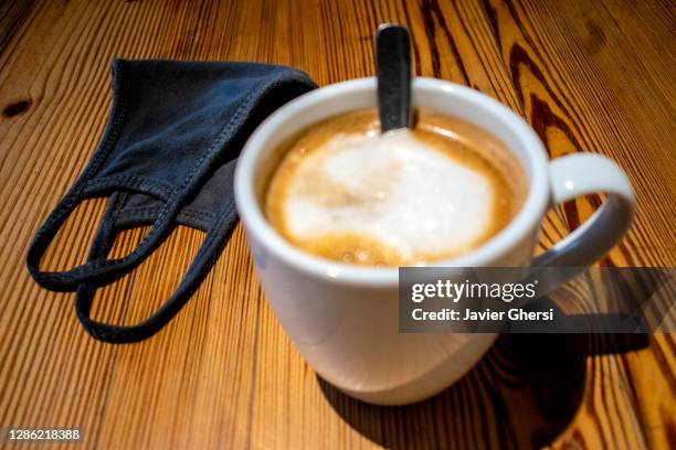 taza de café con leche y tapaboca (barbijo) sobre mesa de madera - mesa de madera bildbanksfoton och bilder