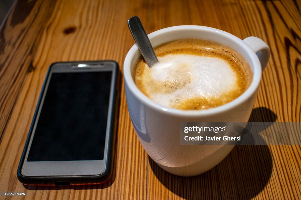 Taza de café con leche y teléfono celular sobre mesa de madera