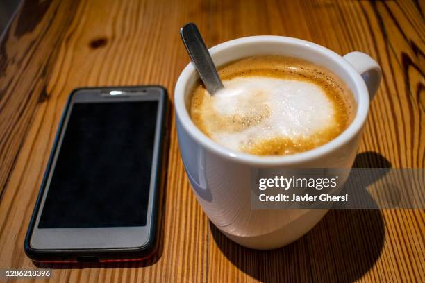 taza de café con leche y teléfono celular sobre mesa de madera - teléfono stock pictures, royalty-free photos & images