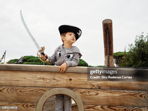 boy in pirate hat of a pirate ship in a playground holding a sword and living an adventure - baby boot stock-fotos und bilder