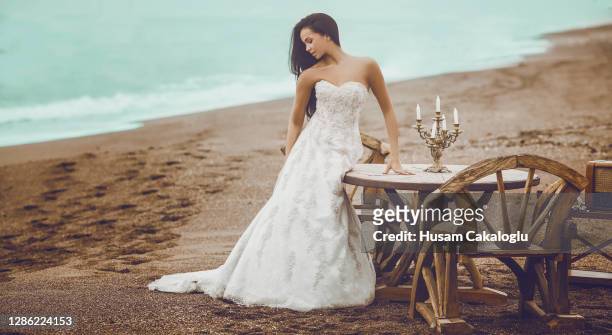 bride waiting for her husband in front of a wooden table with her wedding gown by the beach. - ceremony stock pictures, royalty-free photos & images