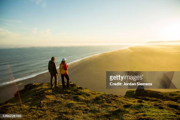 a couple standing on top of a cliff overlooking the ocean in iceland. - activities in the sun stock pictures, royalty-free photos & images