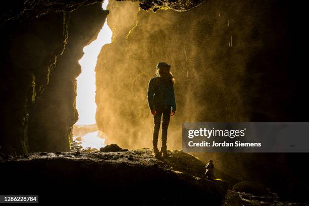 a woman standing in a cave under a waterfall in iceland. - reykjavik photos et images de collection