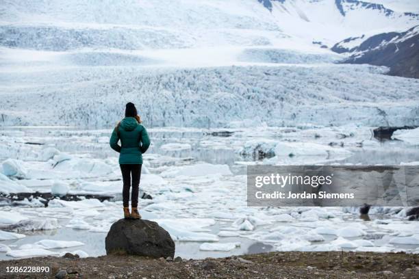 a woman standing on rock in front of a giant glacier in iceland. - reykjavik women stock pictures, royalty-free photos & images