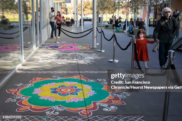 Young girl walks hand-in-hand with a relative while admiring Rangoli, a colorful form of Indian folk art celebrating art, beauty and culture, seen...