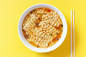 Instant noodle soup in a white bowl on yellow background top view.