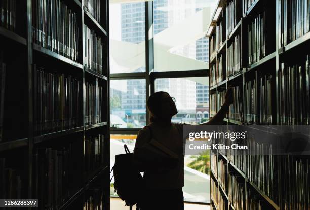 female student in silhouette looking at the books from the bookshelf - campus universidad fotografías e imágenes de stock