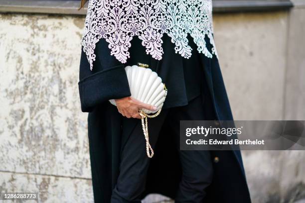 Guest wears a white top with floral embroidery, a black long coat, a white bag in the form of a sea-shell, black pants, outside Paco Rabanne, during...