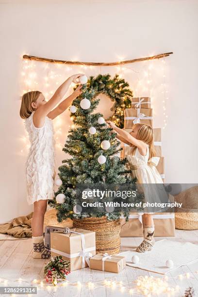 two cute little sisters decorating christmas tree at home - the little white dress stock-fotos und bilder