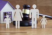Wooden figurines of parents and children stand on table near toy house and judges hammer