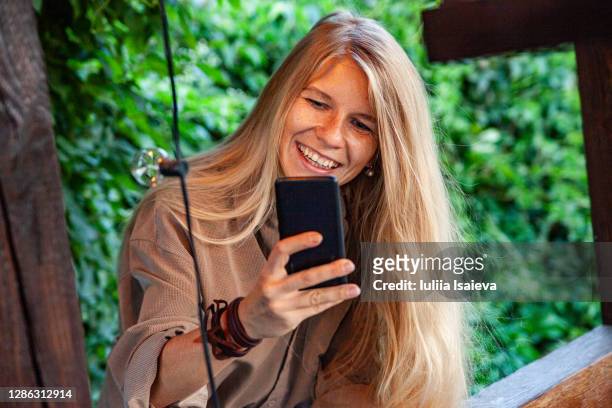 cheerful woman taking photo with smartphone on summer terrace - content stock-fotos und bilder